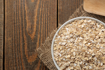 Dry oatmeal in a white bowl and a wooden spoon. food. healthy food. on a brown wooden table.
