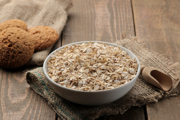 Dry oatmeal and oatmeal cookies in a white bowl and a wooden spoon. food. healthy food. on a brown wooden table.