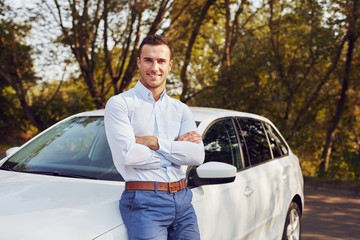 A smiling man with crossed arms stands in front of his new car