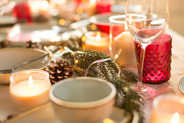 christmas, holidays and decoration concept - pine cone, fir branch and candle burning on table served for festive dinner at home