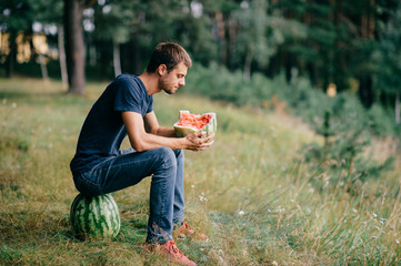 Obraz premium Young odd strange man eating watermelon and drinking its juice at nature. Great delicious taste of summer fruit. Funny adult male fooling with food outdoor in woods. Healthy useful natural nutrition.