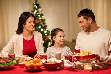 holidays, family and celebration concept - happy mother, father and little daughter having christmas dinner at home