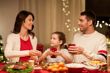 holidays, family and celebration concept - happy mother, father and little daughter with drinks toasting at home christmas dinner