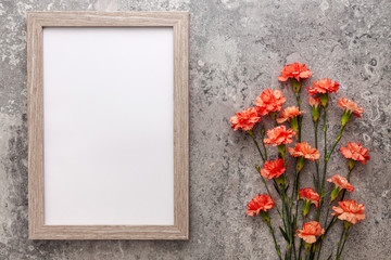 Salmon carnations and wooden empty mockup frame on the background of an old gray concrete wall