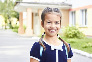 Portrait of little school girl smiling and looking at camera. Happy girl eight years old staying in front of school in uniform. Childhood concept.
