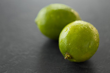 food, healthy eating and vegetarian concept - close up of whole limes on slate table top