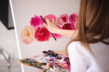 Сute girl artist paints on canvas painting on the easel. Model in the studio