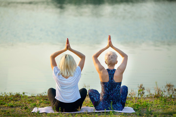 two older women doing yoga near the river in summer