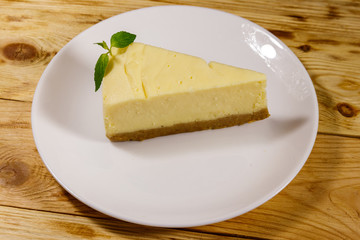 Piece of tasty sweet New York cheesecake in a white plate on wooden table