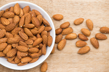 Almonds in a white cup rests on a wooden table