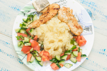 Mashed potatoes with chop and fresh vegetable salad in a plate on wooden background.