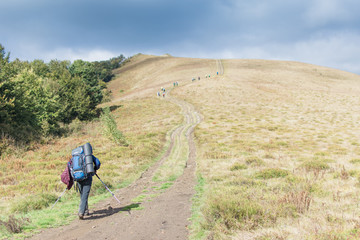 Woman with a large backpack with walking sticks in a hike in the mountains.