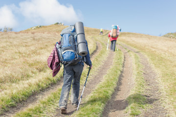 Woman with a large backpack with walking sticks in a hike in the mountains.