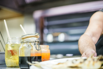 Man preparing fish for barbeque with colorful sauces in foreground