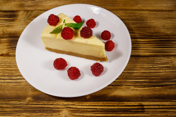 Piece of tasty New York cheesecake with raspberries in a white plate on wooden table