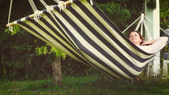 Beautiful woman is lying in hammock in summer and is relaxing