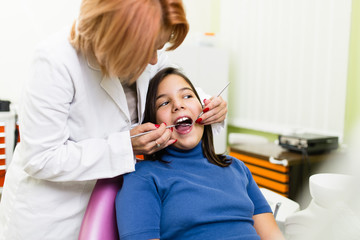 Cute little school girl sitting on dental chair while having dental treatment. Close up shot. Selective focus. Dental health concept.