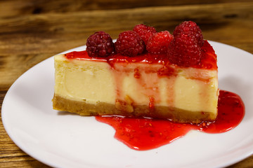 Piece of tasty New York cheesecake with raspberries and raspberry jam in a white plate on wooden table