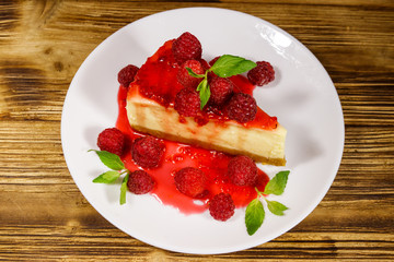 Piece of tasty New York cheesecake with raspberries and raspberry jam in a white plate on wooden table