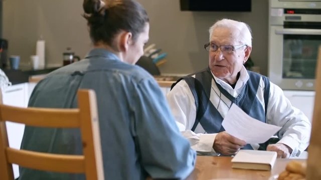 PAN of young man sitting at kitchen table with elderly father in glasses and discussing household bills