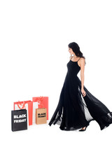 beautiful woman in black dress looking at shopping bags with black friday lettering isolated on...