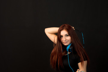 young Redhead woman with blue headphones listening to music od black background
