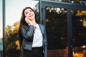 Fototapeta premium Business woman with smartphone close up near office building. Girl have conversation with cell phone. Beautiful caucasian young woman talking with mobile device.