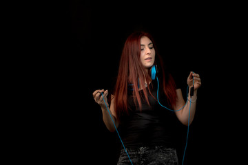 young Redhead woman with blue headphones listening to music od black background