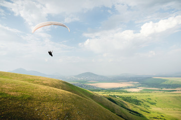 A white-orange paraglider flies over the mountainous terrain