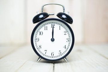 Deadline strait concept with alarm clock set at 12.00 on wooden background.