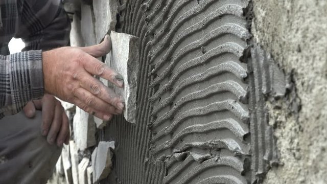 Worker decorating a wall with ornamental stone tiles pressing and fixing a tile firmly into a glue with hammer