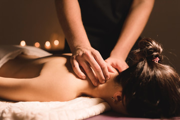 Men's hands make a therapeutic neck massage for a girl lying on a massage couch in a massage spa...