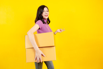 Portrait of the beautiful Asian girl carrying a parcel boxes close up on yellow background. ...