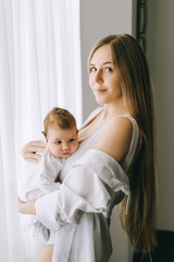 happy mother carrying little baby boy in front of curtains at home