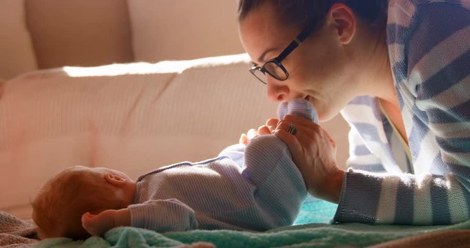 Mother playing with her baby boy feet in living room 4k