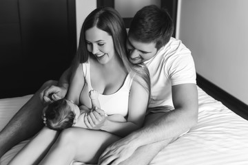 back and white picture of smiling family playing with infant son in bed at home