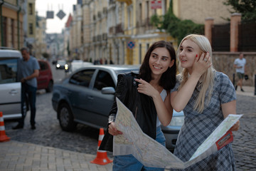 Attractive lesbians holding city map and thinking which place to visit. Spending time together.