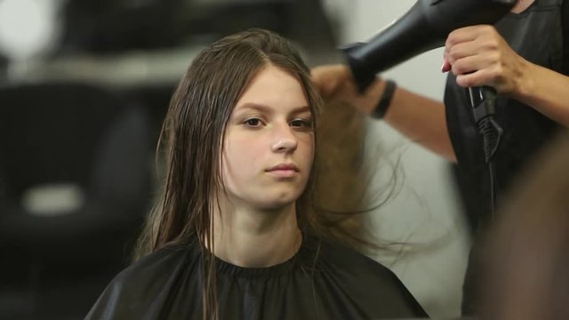 Professional female hair dresser used a hairdryer. Young girl getting her hair dressed in hair salon. Female stylist with a hairdrye