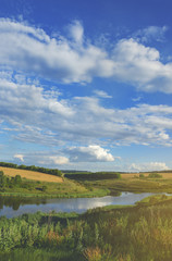 Sunny summer landscape with river,fields,green hills and beautiful clouds in blue sky.