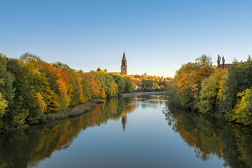 Beautiful fall foliage and Aura river against clear blue sky with Turku Cathedral in background in...