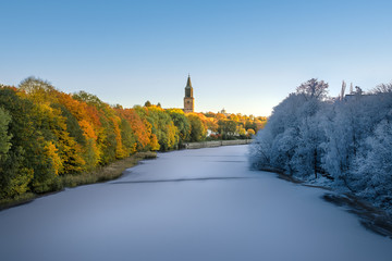 Transition image from autumn to winter in single image with frozen river and colorful fall foliage and Turku Cathedral in background