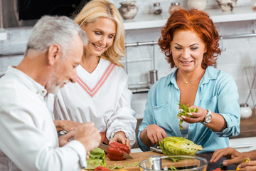 smiling mature friends preparing healthy detox salad for dinner at home