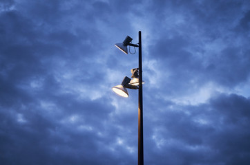 Farola encendida delante de un cielo azul nuboso de tormenta