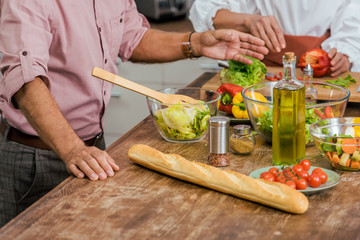 cropped image of couple preparing salad for dinner at home