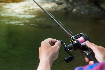 Fishing reel multiplier with a fishing rod in the hands of the fisherman. Trout fishing in the...