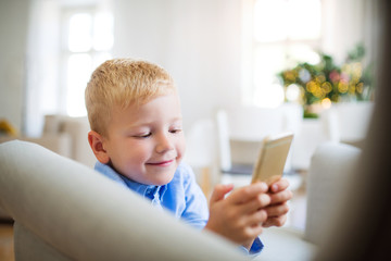 A small boy with smartphone sitting on an armchair at home at Christmas time.