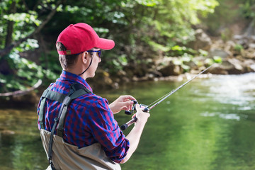 Man fisherman catching trout in the river fishing rod. Fly fishing in a forest creek in Europe. Professional sport angler catches a fish.