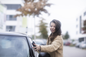 Junge Frau mit Smartphone checkt Carsharing Auto