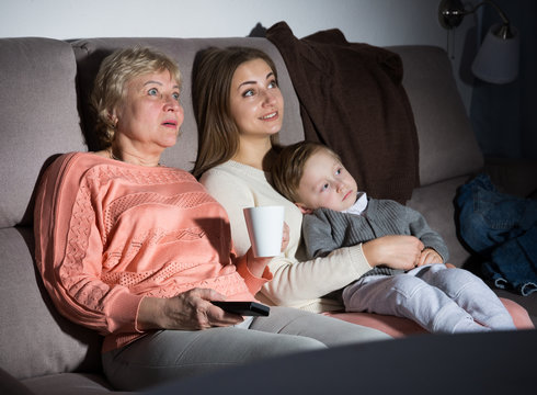 Woman with her mother and son are watching film in time evening rest