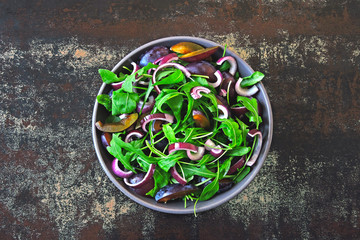 Obraz na płótnie Canvas Healthy salad with arugula, plum and blue onions in a bowl on a stylish shabby background. Vegan bowl with plum salad. Arugula plum salad. The concept of proper nutrition.
